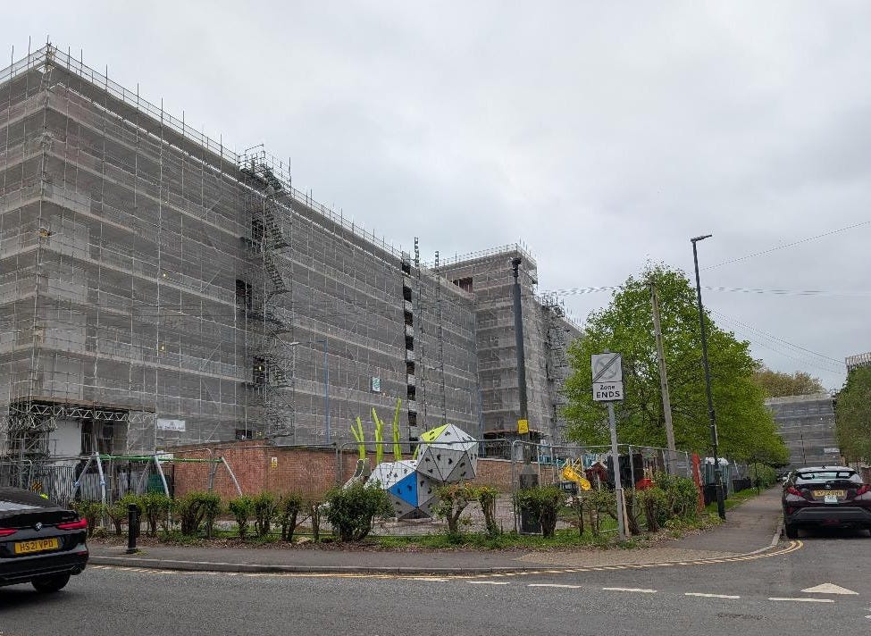 Exterior view of high-rise council flats in St Jude’s, Bristol, encased in scaffolding and safety catch-nets. The image shows Charleton House during PAS 2035 thermal efficiency window installation amid ongoing structural deficiency inspections and Building Safety Act compliance reviews-thealmightygob.com