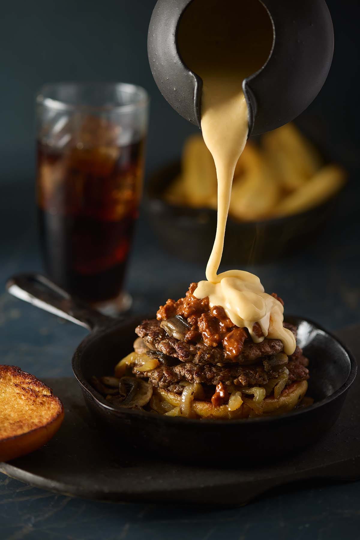 A detailed close-up of velvety cheddar cheese sauce being poured, highlighting its smooth and creamy texture.