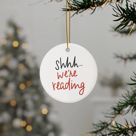 Silent Book Club merchandise on sale includes an Introvert Happy Hour T-shirt, Sorry I'm Booked hoodie, Audiobook lover sweatshirt, Silent Book Club logo sticker, Read with Friends wooden ornament, and Shh we're reading ceramic ornament
