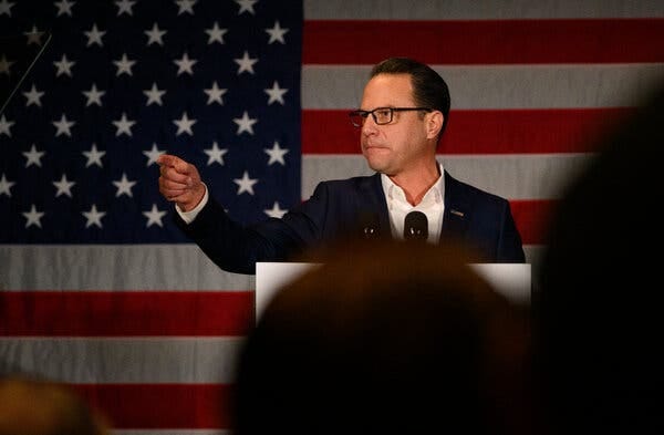 Josh Shapiro standing and pointing in front of an American flag during a speech.