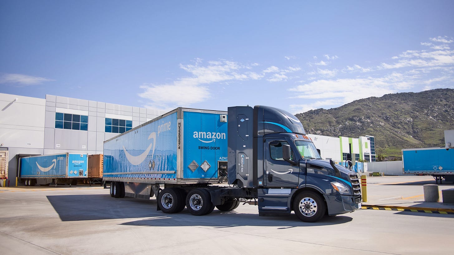 Um caminhão da Amazon Prime com um reboque azul estacionado em um centro de distribuição com colinas e céu limpo ao fundo. Um caminhão da Amazon Prime com um reboque azul estacionado em um centro de distribuição com colinas e céu limpo ao fundo.