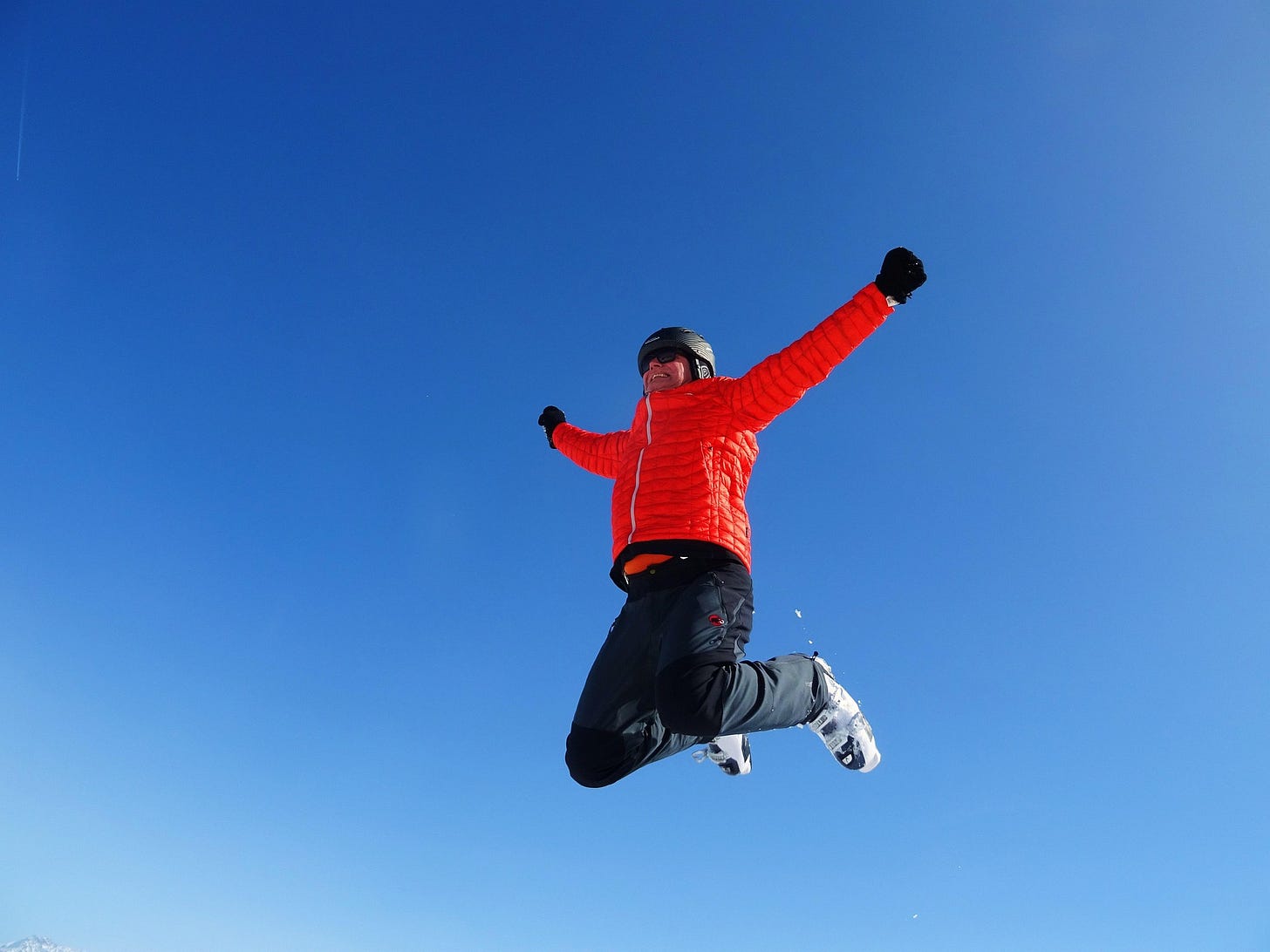 Person in a bright orange ski jacket and helmet jumps high against a vivid blue sky, arms outstretched. A joyful leap of faith—midair, mid-decision, and fully committed. Person in a bright orange ski jacket and helmet jumps high against a vivid blue sky, arms outstretched. A joyful leap of faith—midair, mid-decision, and fully committed.