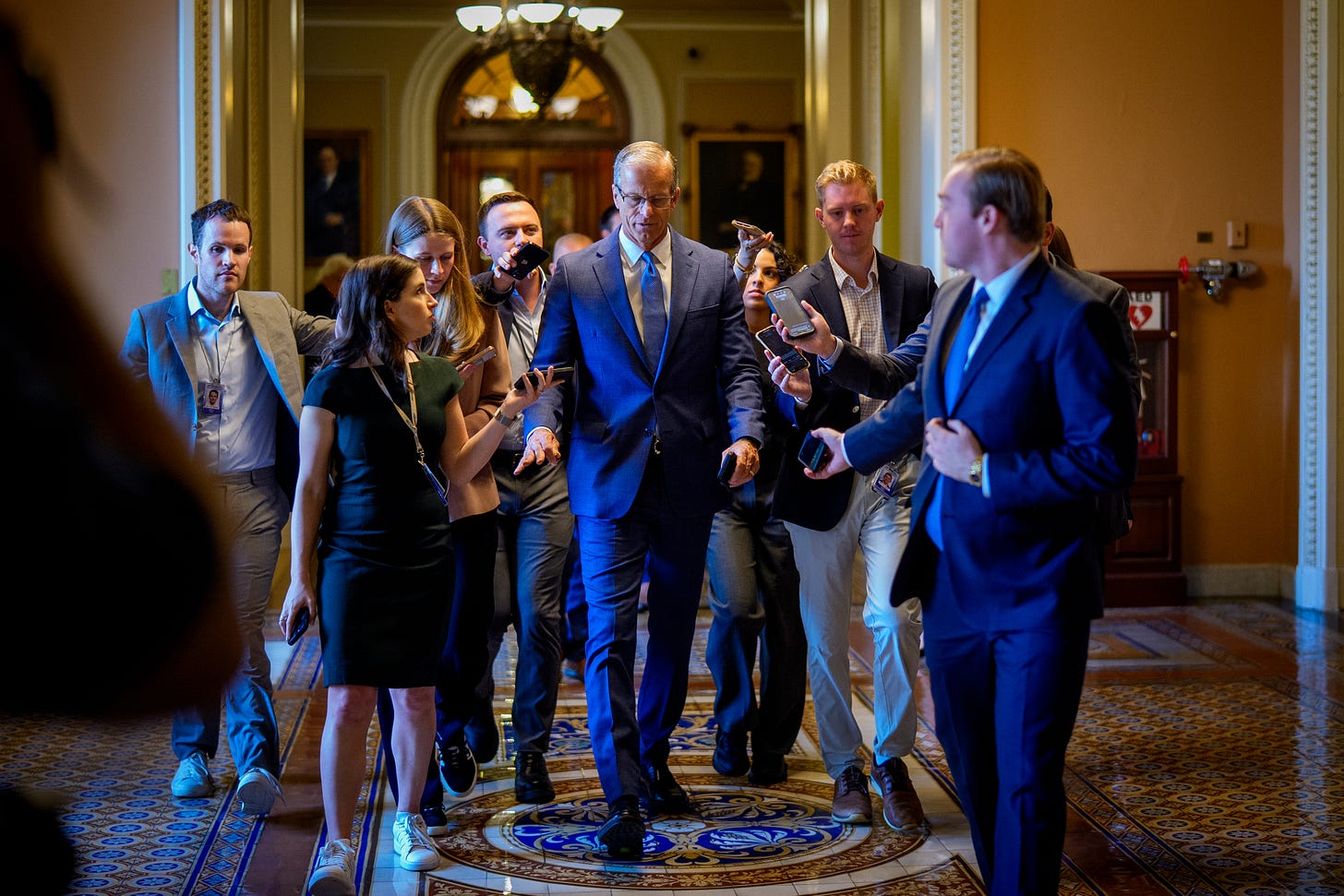 A group of people in suits walking down the hallway, including Senate Majority Leader John Thune.
