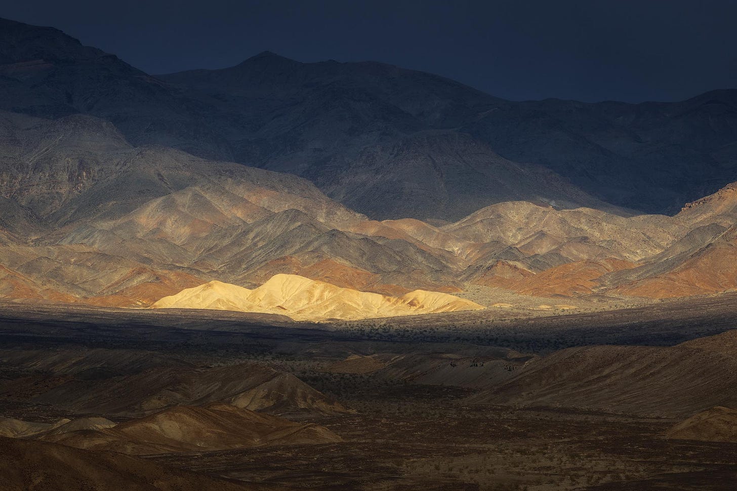 Fleeting Warm light illuminates a small white hill for a few moments as a storm passes through Death Valley National Park.