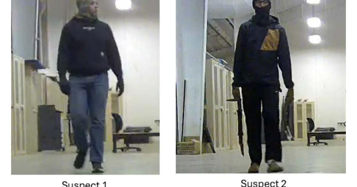 Surveillance image showing two suspects walking in a dimly lit indoor space, one holding an object resembling a weapon.
