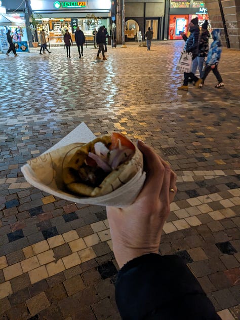 Author in front of the sea, holding a gyro, and with my new friend in front of a restaurant.