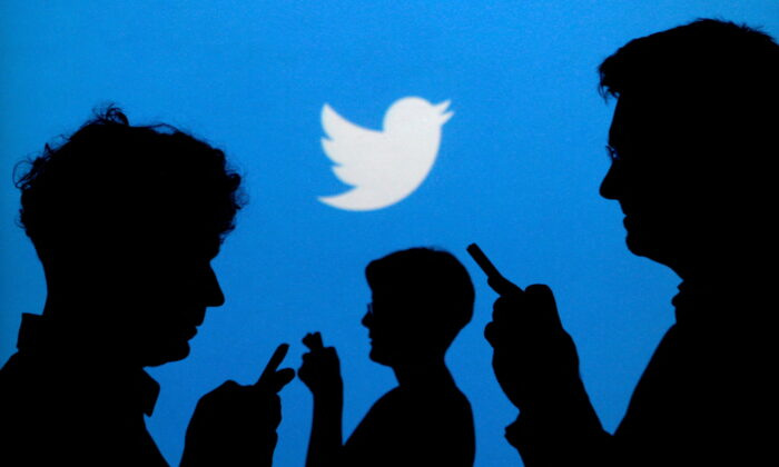 People holding mobile phones are silhouetted against a backdrop projected with the Twitter logo in this illustration picture taken on Sept. 27, 2013. (Kacper Pempel/Illustration/Reuters)