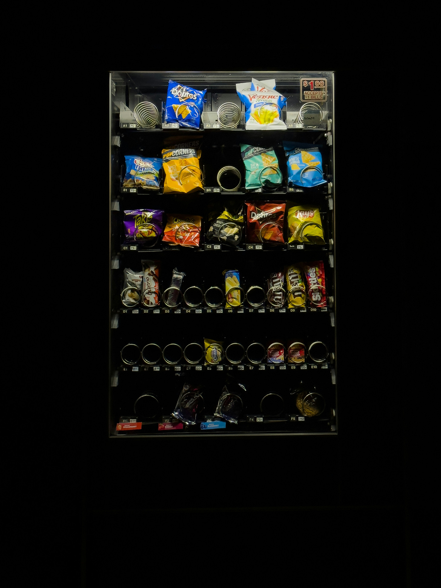 A snack vending machine is filled with crisps and candy, some slots are empty.