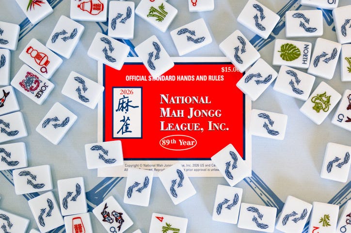 Real mahjong tiles arranged around the closed 2026 NMJL card on a blue table covering. Real mahjong tiles arranged around the closed 2026 NMJL card on a blue table covering.