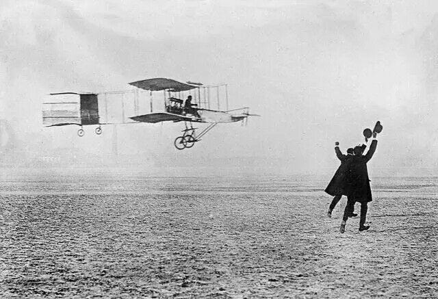 This may contain: an old photo of a man flying a plane in the sky with two people on it