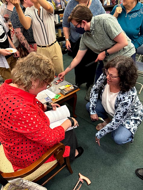 1.A cake decorated with a bridge and cityscape, with “Echoes of the  Lost” written in red across it. 2. Cindy signing books for a crowd lined up next to her. 3. Cindy holding a bunch of asparagus as if it were a bouquet,