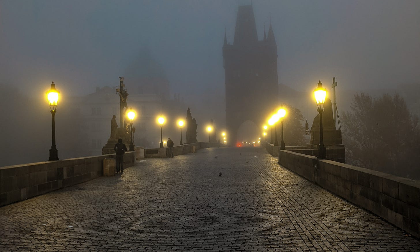 Charles Bridge lit up by lamps on a foggy morning