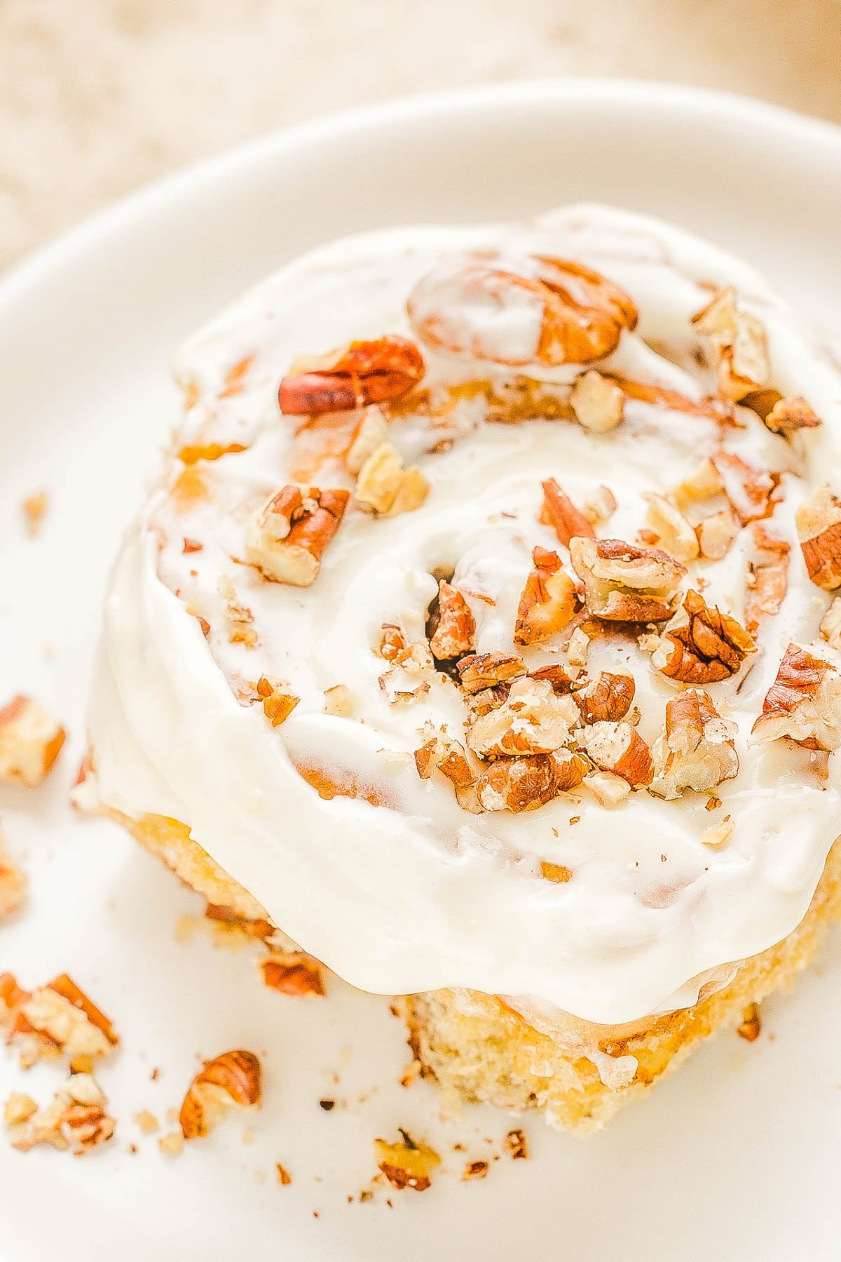 Cinnamon roll with cream cheese frosting and chopped pecans on a white plate.