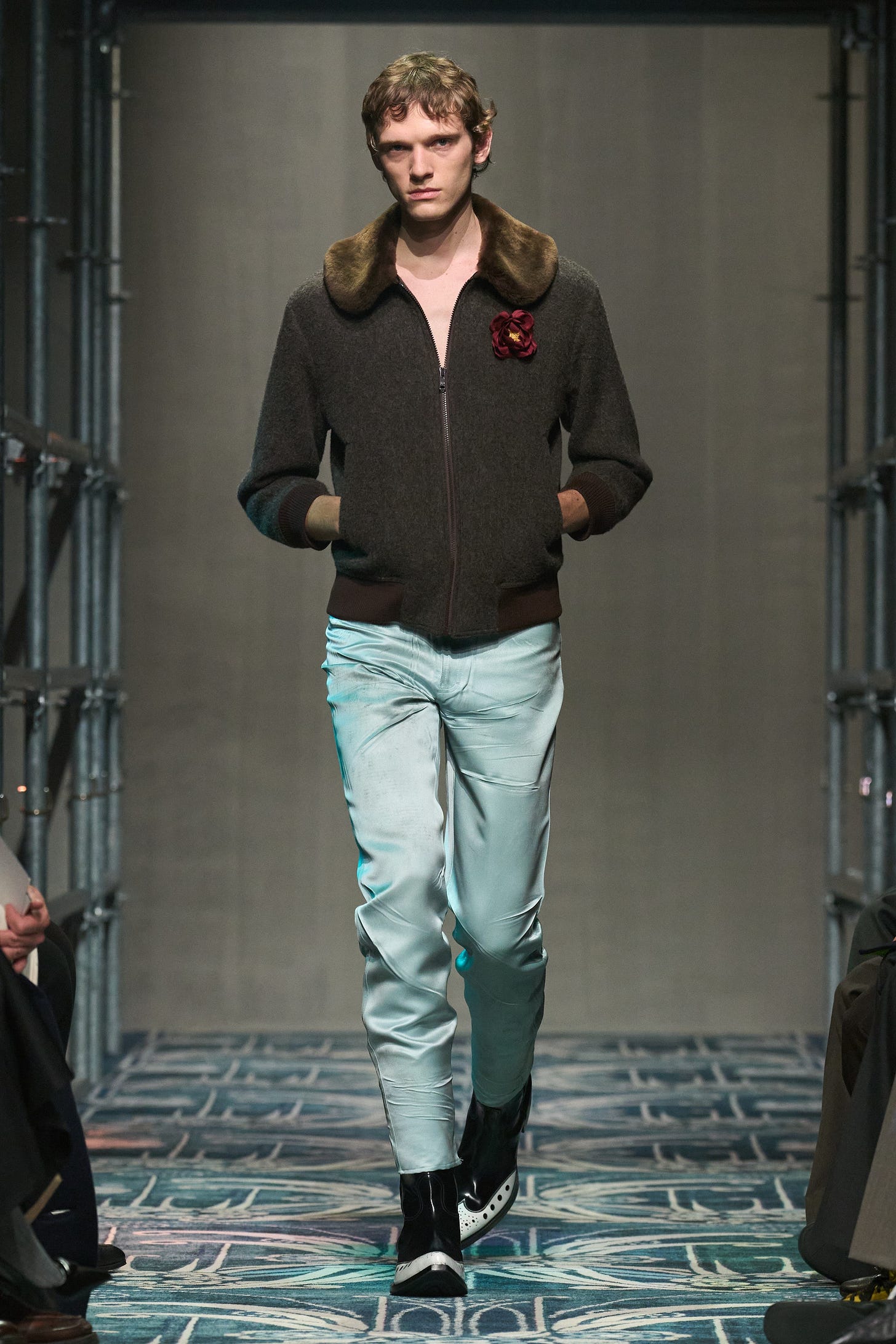 A model walks the runway wearing a shruken gray sweater with a fur collar, ice blue satin pants and coyboy boots.