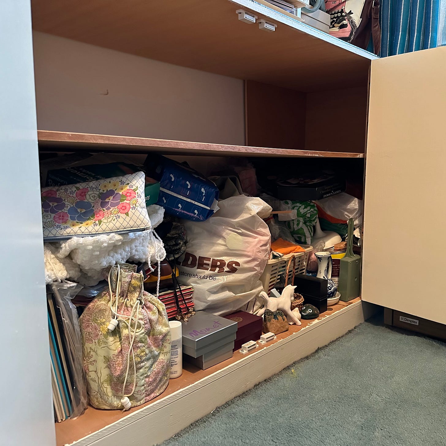 Cupboard, the top shelf completely empty, the bottom one full to the brim of tat.