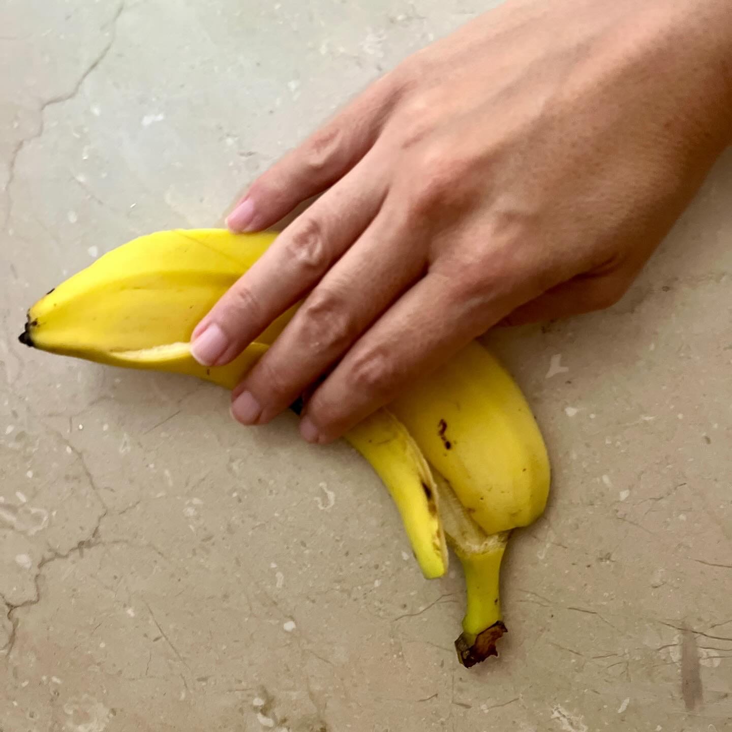 a hand holding a banana peel against a marble wall
