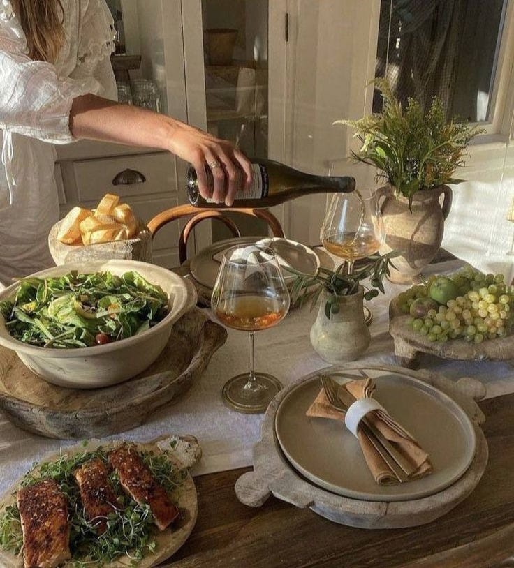 This may contain: a woman pouring wine into a glass on top of a table filled with plates and bowls This may contain: a woman pouring wine into a glass on top of a table filled with plates and bowls