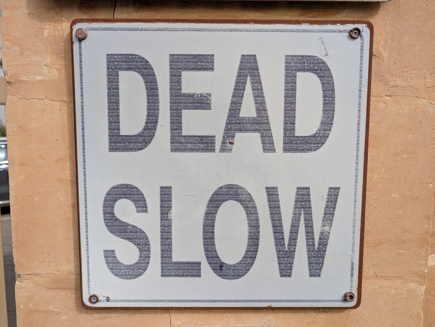 Traffic sign on a wall reading "DEAD SLOW"