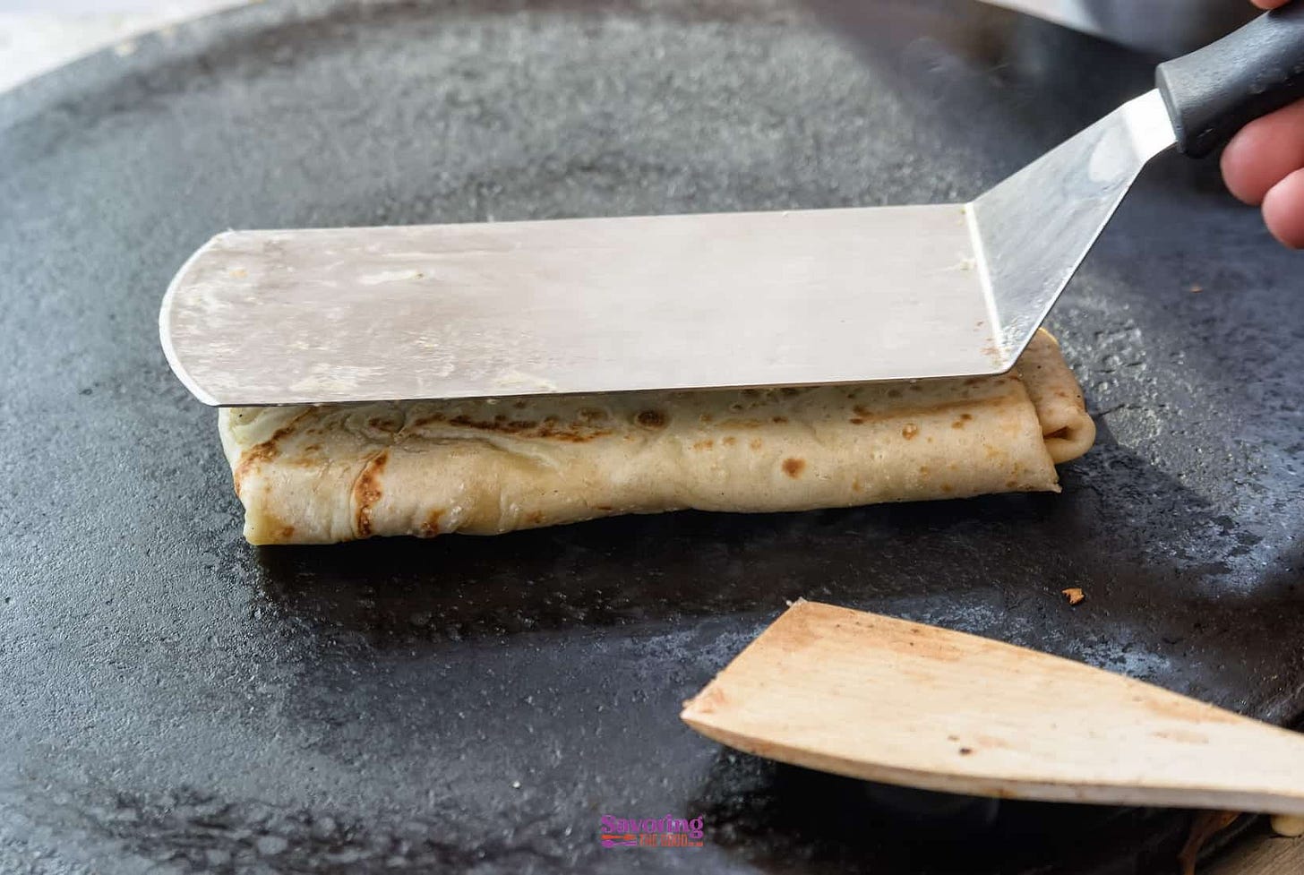 A person is making a crepe on a frying pan.