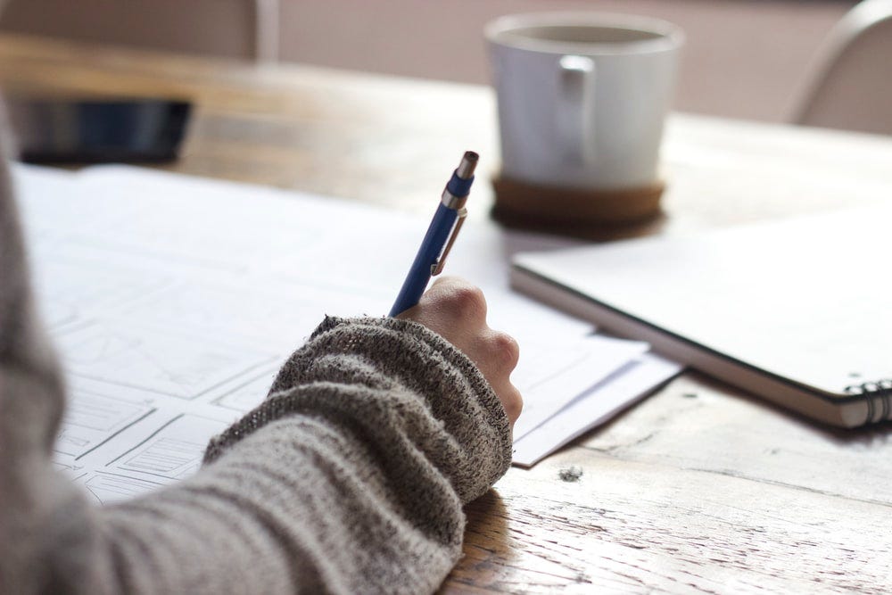 person writing on brown wooden table near white ceramic mug person writing on brown wooden table near white ceramic mug