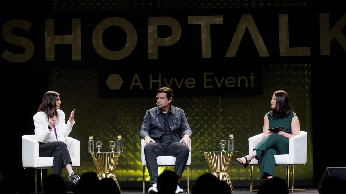 Three people sit on chairs on a stage with the word "Shoptalk" in the background.