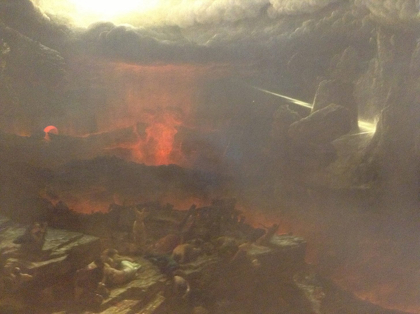 A vast dark landscape under a black sky split by lightning, with a ruined town on rocks and tiny crowds fleeing, while in the foreground a standing man raises his arms with broken chains at his wrists.