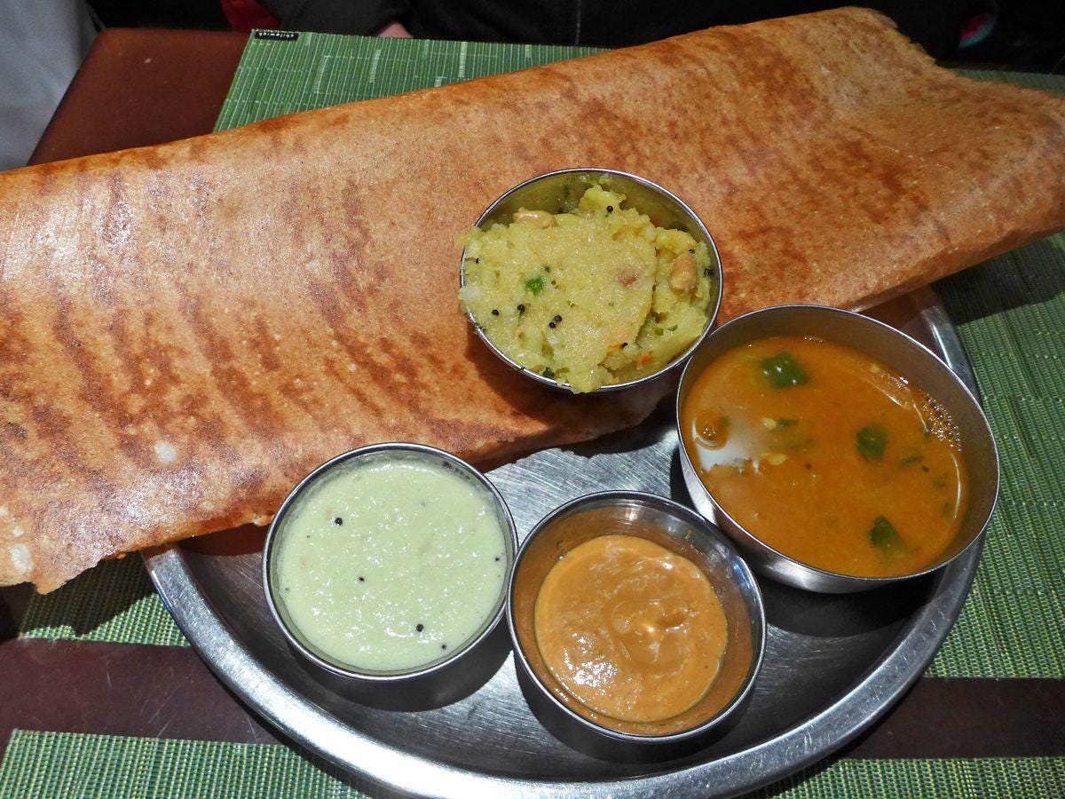 A flat folded crepe with a tub of potatoes on top and three sauces on the side.