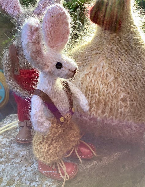 Knitted toys under a red rose bush surrounded by fallen petals