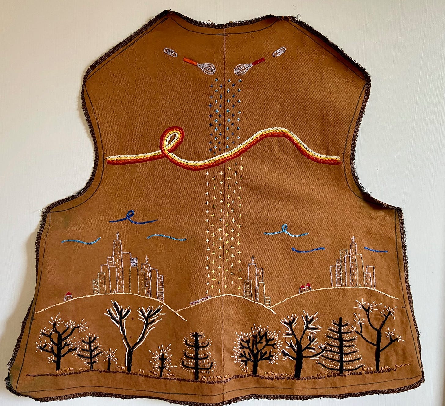 A piece of fabric embroidered with whisks, swirls, a cityscape, and a forest