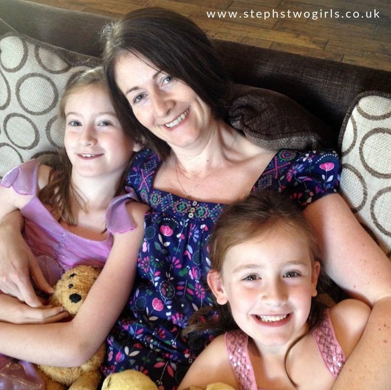 mum with brown hair smiling at camera with her arms around her two young daughters, also smiling at the camera mum with brown hair smiling at camera with her arms around her two young daughters, also smiling at the camera