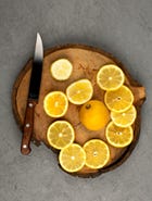 A sliced lemon on a wooden board next to a sharp knife.
