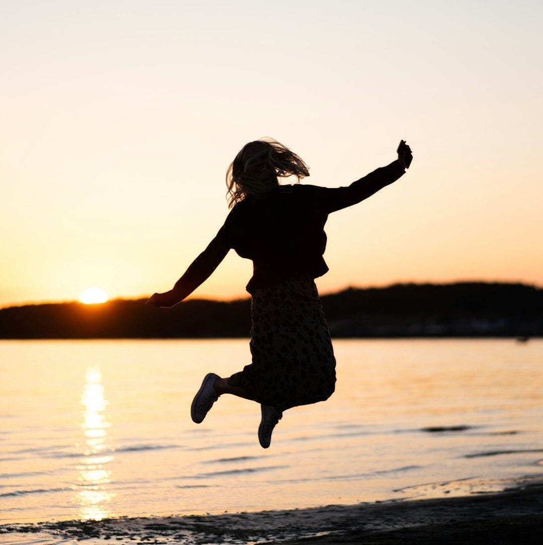 girl in black dress jumping on water during sunset