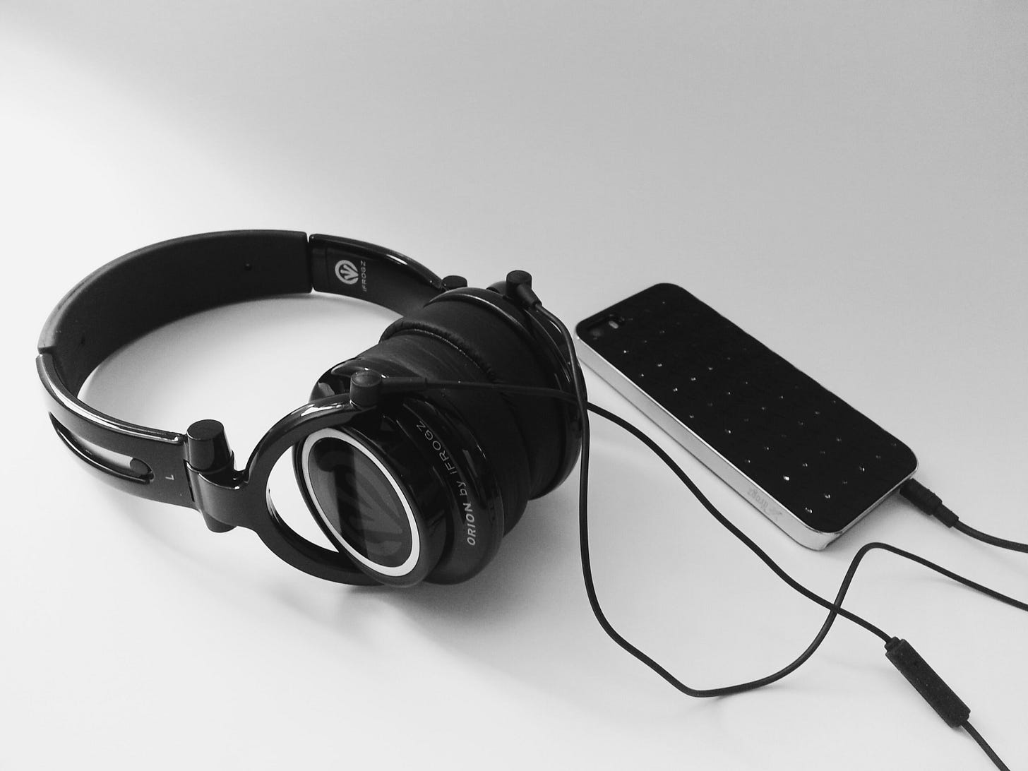 Black and white photo of black headphones and an old iPhone turned down so you can see its black case
