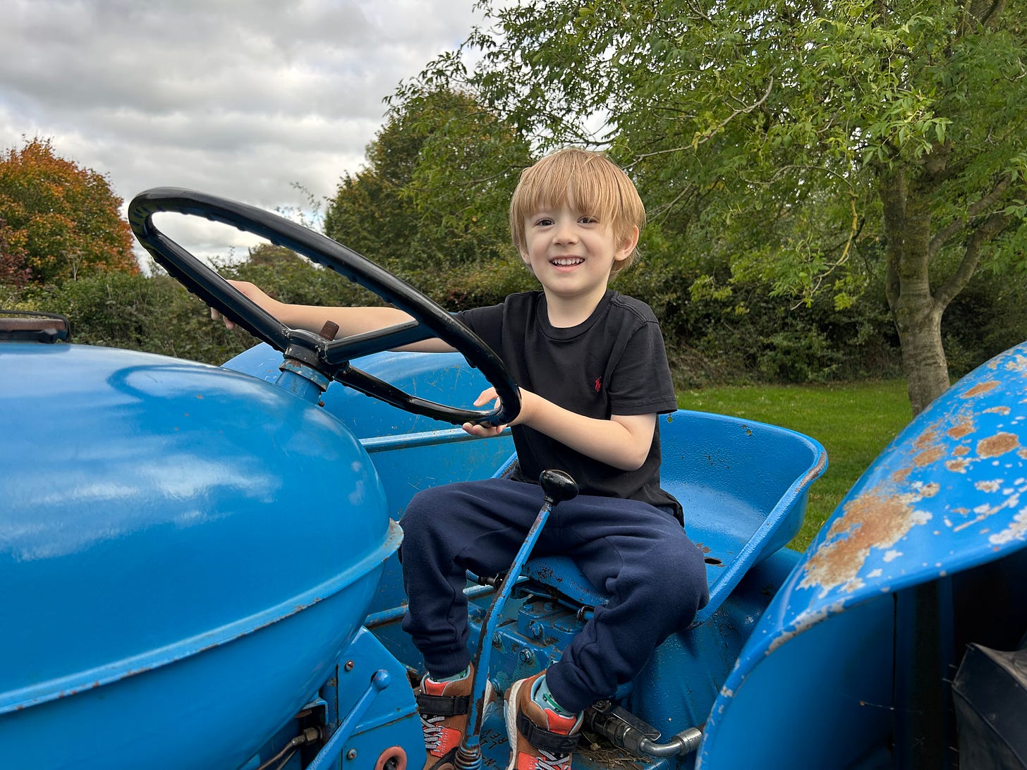 A blue tractor with a boy enjoying acting as a driver. Hartley Farm Winsley, Bradford on Avon, Wiltshire