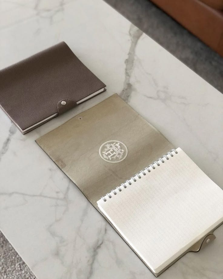 This may contain: two notebooks on a marble table with a leather wallet next to one that is empty