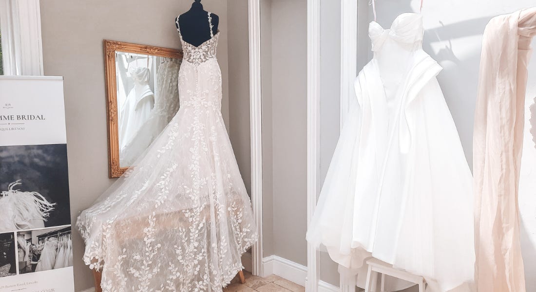 Two bridal dresses next to a grey wall and banner Two bridal dresses next to a grey wall and banner