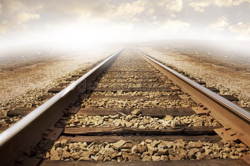Railroad tracks on a bed of rock stretching out across parched dry landscape. Cloudy background with strong lighting to the left of the image. Concept for exploration or adventure into the unknown. Destiny stock images, royalty-free photos and pictures