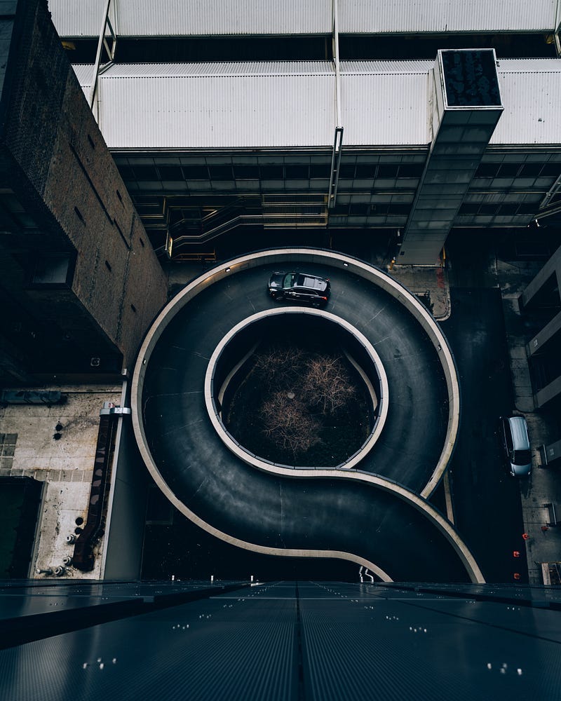 A parking circular parking garage on-ramp is seen from above, with a single car driving along it. A parking circular parking garage on-ramp is seen from above, with a single car driving along it.