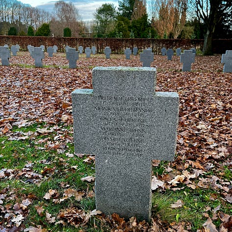 Gravestone with branches of different colored evergreens; neat plots linedwith gravel and divided by small hedges; a granite cross etched with many names