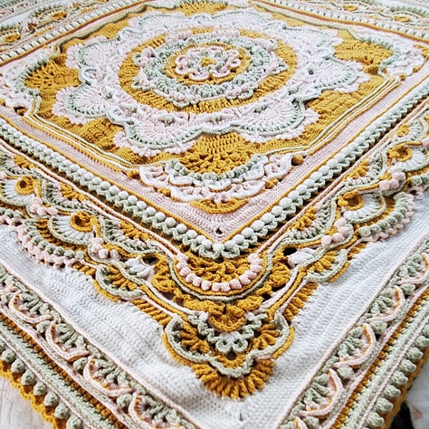 A crocheted mandala afghan blanket in goldenrod, sage, pink, and white.