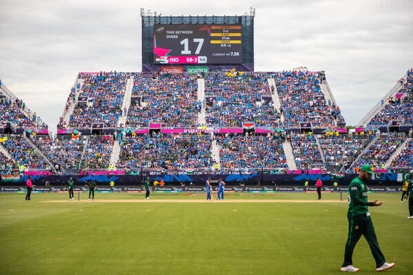 Cricket players walk on the field with spectators in the background.
