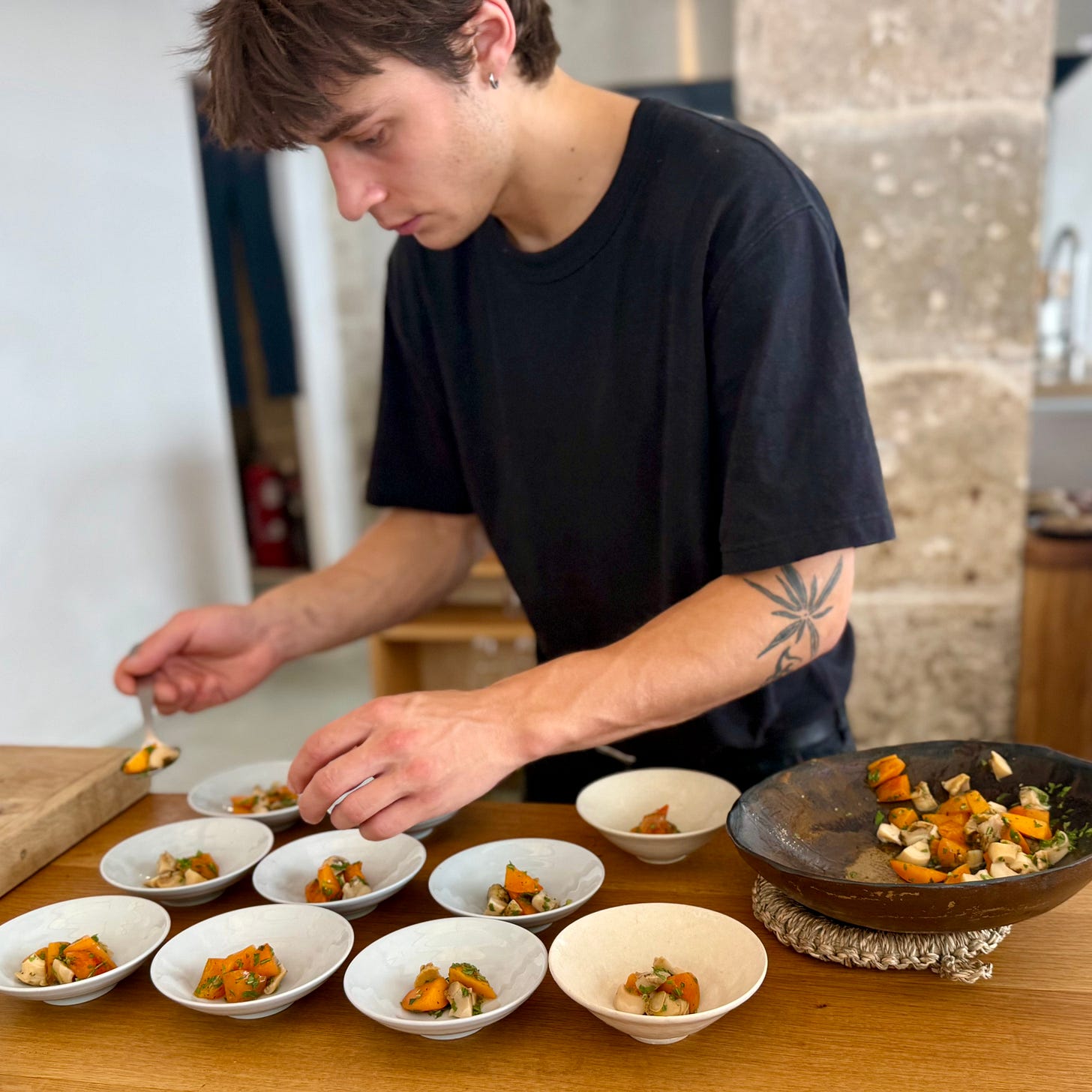 A cook plating a shellfish course on beds of salt at the oak table at Bittikesu, Paris 4th A cook plating a shellfish course on beds of salt at the oak table at Bittikesu, Paris 4th