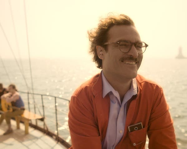 A smiling man in an orange jacket stands on boat with a device peeking out from a chest pocket.