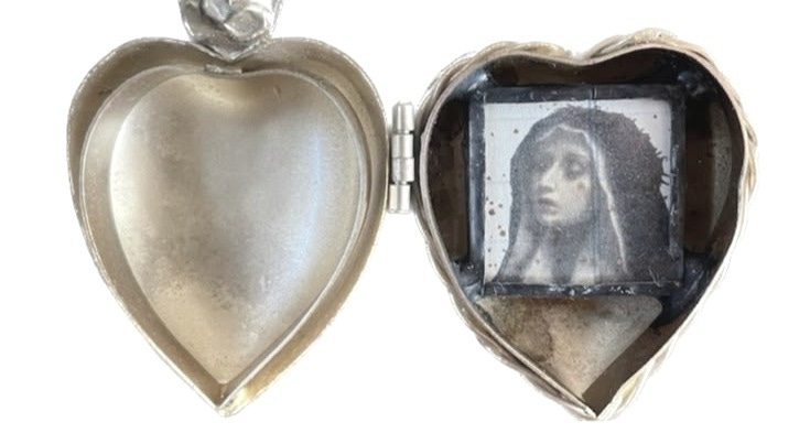 This may contain: a silver heart shaped box with a painting in the shape of a woman's face