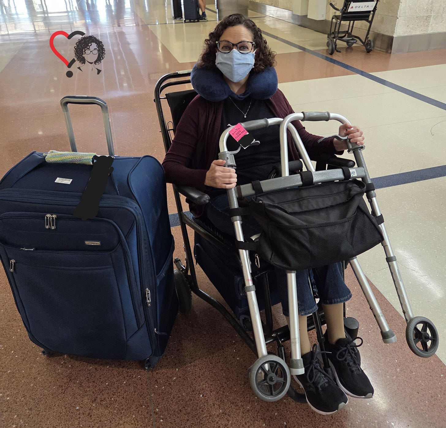 Writer in airport wheelchair. She is wearing glasses and a mask. She is balancing a walker and a cane on her lap. There is a large suitcase to her right. Photo credit: M. Rafson