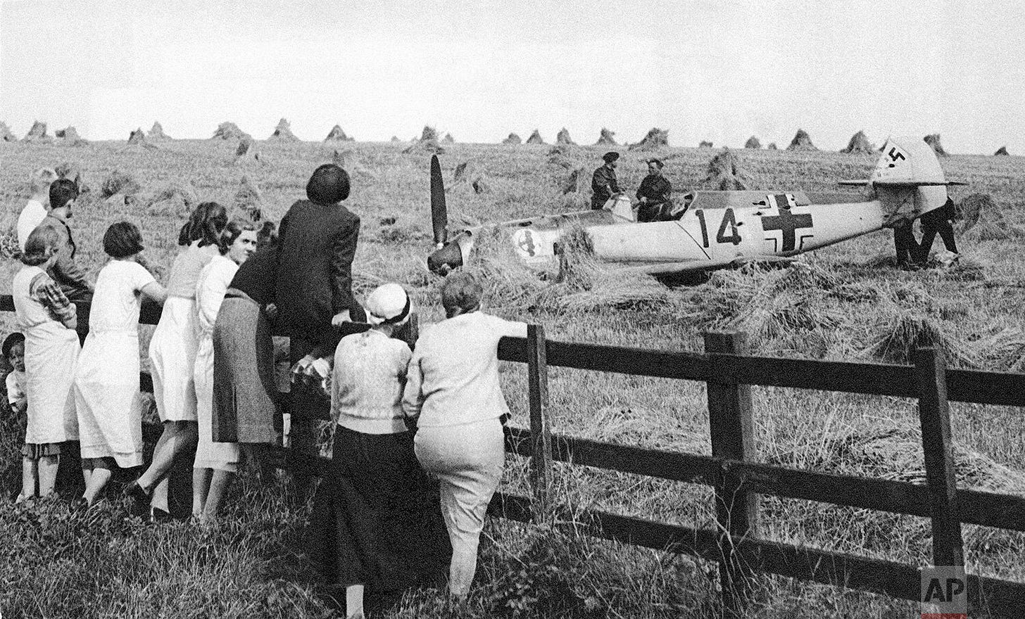 British women gather to view a shot-down Messerschmitt fighter in a wheat field near Berwick on August 19, 1940, a testament to the aerial battles raging during the Battle of Britain.