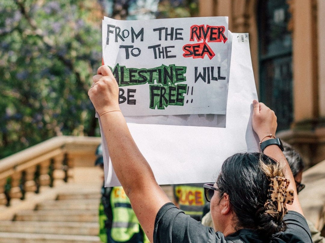 a man holding a sign that says from the river to the sea a man holding a sign that says from the river to the sea