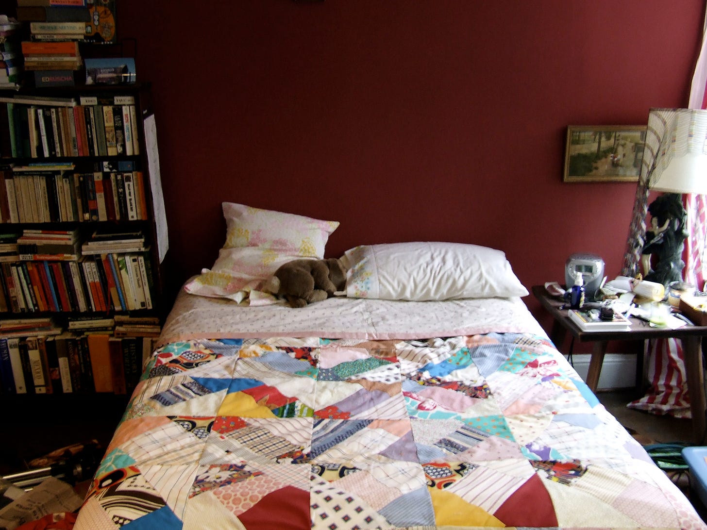 bedroom scene with handmade quilt on bed and bookself full of books