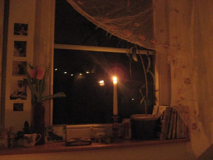 This may contain: a candle is lit in front of a window with curtains on the windowsills