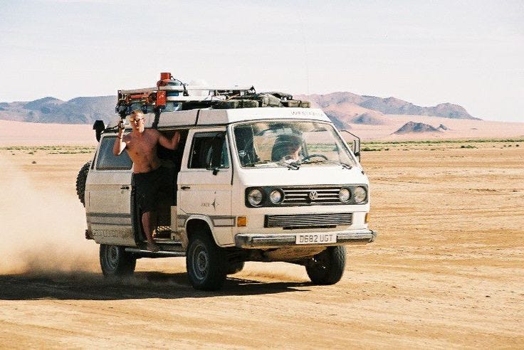 This may contain: a man standing in the back of a white van on top of a dirt field This may contain: a man standing in the back of a white van on top of a dirt field